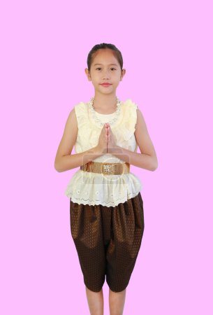 Sauberes asiatisches Mädchen in traditioneller thailändischer Kleidung mit Respekt, Sawasdee-Symbol, Willkommensausdruck auf rosa Hintergrund, Vorderansicht und Schnittweg.