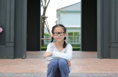 Téléchargez les photos : Portrait de jeune fille asiatique portant des lunettes avec caméra de regard tout en étant assis dans le jardin. - en image libre de droit
