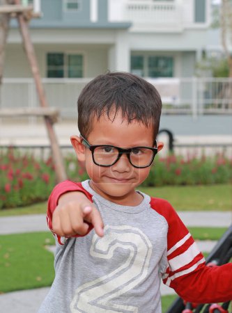 Téléchargez les photos : Portrait de petit garçon asiatique pointant droit sur vous et portant des lunettes pendant votre séjour dans le jardin. - en image libre de droit