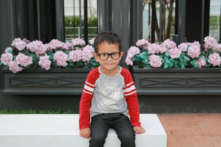 Téléchargez les photos : Asiatique petit garçon enfant portant des lunettes tandis que assis dans le jardin. - en image libre de droit
