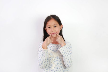 Téléchargez les photos : Portrait de jeune fille asiatique gardant les doigts sur le coin de la bouche isolé sur fond blanc. Pointe de l'enfant sur la partie du corps. - en image libre de droit