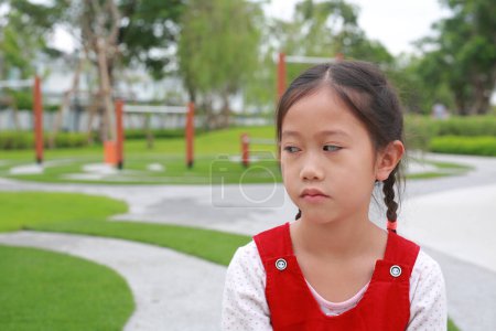 Téléchargez les photos : Malheureux avec le visage ennuyé de fille asiatique enfant avec regarder à côté tandis que rester dans le jardin. - en image libre de droit