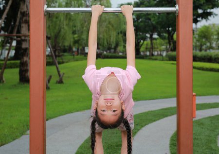 Asiatique fille enfant profiter à accrocher à l'envers sur la clôture en aluminium dans le parc public.