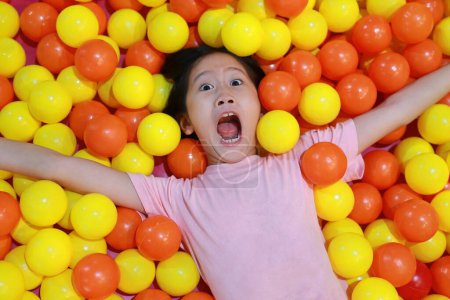 Téléchargez les photos : Excité asiatique jeune fille tout en jouant à coloré plastique balles aire de jeux. - en image libre de droit