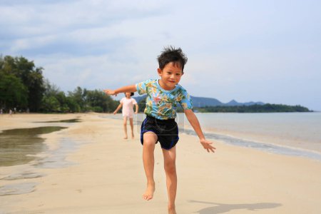 Téléchargez les photos : Heureux petit garçon asiatique enfant et fille enfant s'amusant à courir sur la plage de sable tropical au lever du soleil. Bonne famille sœur et frère profiter des vacances d'été. - en image libre de droit