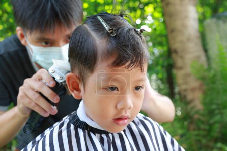 Téléchargez les photos : Cutting hair of Asian little boy with Hair Clipper in the garden - en image libre de droit