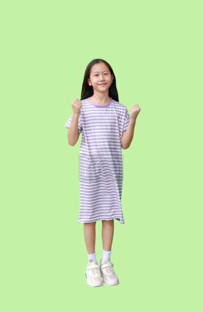Téléchargez les photos : Portrait de fille asiatique enfant montrant gagnant lever les poings sourire geste isolé sur fond vert. Image pleine longueur avec le chemin de coupe. - en image libre de droit