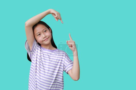 Téléchargez les photos : Asiatique fille enfant montrant à l'espace de copie avec pointant vers le haut et vers le bas et regarder à côté de publicités sur cyan. Image avec chemin de coupure. - en image libre de droit