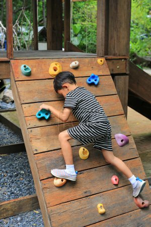 Téléchargez les photos : Asiatique petit garçon âge environ 5-6 ans essayer de monter sur l'équipement de planche en bois à aire de jeux. - en image libre de droit