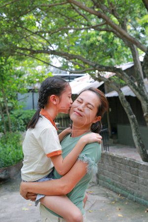 Téléchargez les photos : Happy famille asiatique fille enfant baiser sur la joue sa mère tandis que dans le jardin naturel. Mère portant fille. - en image libre de droit