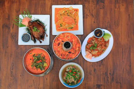 Varieties of Thai food on wooden table background. Tom Yum. Periwinkle curry. Pork bones soup. Stir fried crab. Sliced roast duck. Grilled Peking Duck. Top view.