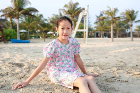 Téléchargez les photos : Souriant asiatique jeune fille enfant se détendre sur la plage de sable et de la caméra à la recherche de vacances d'été. - en image libre de droit