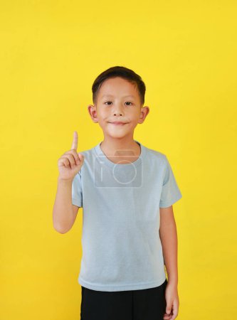 Téléchargez les photos : Asiatique petit garçon gosse montrant index ou un index et regardant droit tout en se tenant isolé sur fond jaune. - en image libre de droit