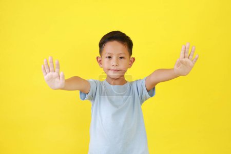 Téléchargez les photos : Portrait de garçon asiatique enfant montrent signe stop geste isolé sur fond jaune. Enfant montrant la paume. - en image libre de droit