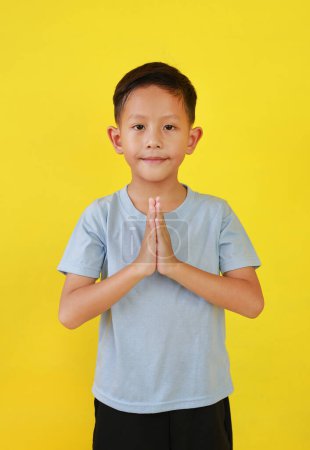 Porträt eines asiatischen Jungen im Alter von etwa 6 Jahren Respekt zollen oder Gebetsgeste isoliert auf gelbem Hintergrund.