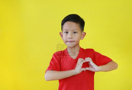 Téléchargez les photos : Portrait de garçon asiatique heureux avec un symbole en forme de coeur avec les mains isolées sur fond jaune. - en image libre de droit