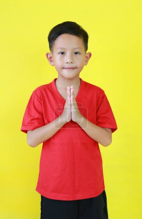 Porträt eines asiatischen Jungen im Alter von etwa 6 Jahren Respektgeste und Blick direkt in die Kamera isoliert auf gelbem Hintergrund.