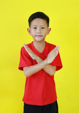 Asiatique garçon enfant en rouge casual âge 7 ans croisé ses mains geste isolé sur fond jaune. Joyeux signe d'arrêt d'exposition d'enfant ou faisant des bras de signe X et caméra regardante.