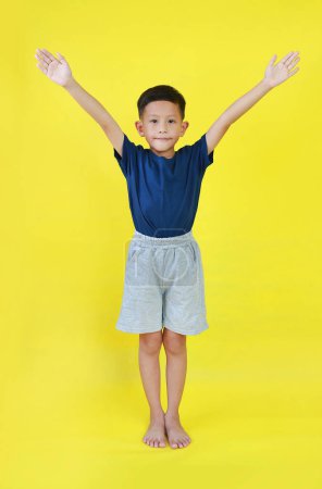 Téléchargez les photos : Asiatique garçon enfant levé les mains. Enfant debout et levez les bras isolés sur fond jaune. Image pleine longueur. - en image libre de droit
