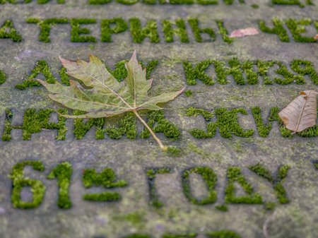 Téléchargez les photos : Feuille d'automne sur une pierre tombale avec le texte écrit en cyrillique - en image libre de droit