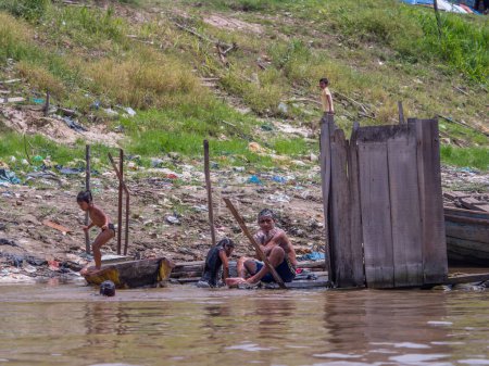 Photo for Iquitos, Peru - Sep 25, 2018: Family is taking a bath in the  Itaya River. A huge pollution can be seen in the background. Low water season of Amazon. Beln district of Iquitos Peru - Royalty Free Image