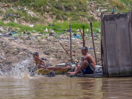 Téléchargez les photos : Iquitos, Pérou - 25 sept. 2018 : La famille prend un bain dans la rivière Itaya. Une énorme pollution peut être vue en arrière-plan. Basse saison des eaux de l'Amazonie. Quartier Beln d'Iquitos Pérou - en image libre de droit