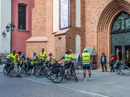 Téléchargez les photos : Varsovie, Pologne - 02 juin 2017 : Cyclistes en gilets jaunes sur la place de la Vieille Ville (Rynek Stare Miasto) pendant l'heure d'été, site du patrimoine mondial de l'UNESCO. - en image libre de droit
