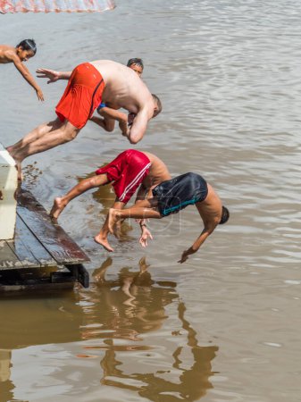 Téléchargez les photos : Pebas, Pérou - 04 décembre 2018 : Des enfants péruviens sautent sur le rover amazonien avec un grand homme blanc. Concept de diversité - en image libre de droit