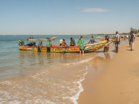 Photo for Nianing, Senegal - January 2, 2019: Fishermen collecting fish from colored wooden fisher boat standing on the beach. Africa - Royalty Free Image