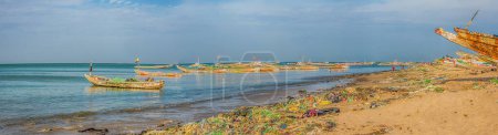 Photo for Senegal, Africa - January 26, 2019: Plenty of plastic bags on shore of the ocean. Pollution concept. Colorful fisher boats in the background. Panoramoc view. Senegal. Africa. - Royalty Free Image
