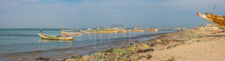 Téléchargez les photos : Sénégal, Afrique - 26 janvier 2019 : Plein de sacs plastiques sur le rivage de l'océan. Concept de pollution. Des bateaux de pêche colorés en arrière-plan. Vue panoramique. Sénégal. Afrique. - en image libre de droit