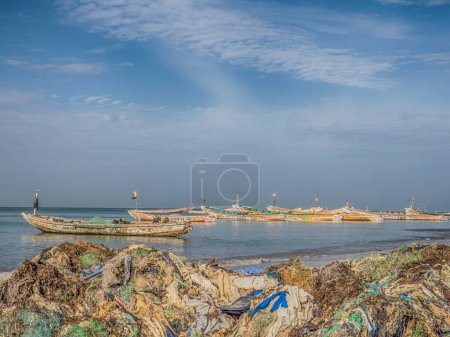 Téléchargez les photos : Sénégal, Afrique - 26 janvier 2019 : Plein de sacs plastiques sur le rivage de l'océan. Concept de pollution. Des bateaux de pêche colorés en arrière-plan. Sénégal. Afrique. - en image libre de droit