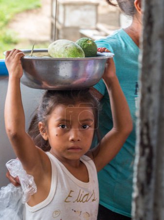 Téléchargez les photos : Petit village près du fleuve Amazone, Pérou - 03 déc. 2018 : Travail des enfants. Petite fille vendant les fruits sur le ferry-boat nageant de Santa Rosa à Iquitos sur le fleuve Amazone - en image libre de droit