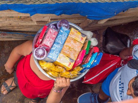 Téléchargez les photos : Petit village près du fleuve Amazone, Pérou - 03 déc. 2018 : Travail des enfants. Petite fille vendant des bonbons sur le ferry nageant de Santa Rosa à Iquitos sur le fleuve Amazone - en image libre de droit