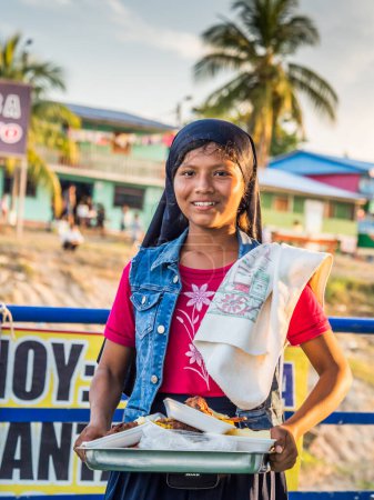 Téléchargez les photos : Petit village près du fleuve Amazone, Pérou - 03 déc. 2018 : Travail des enfants. Fille vendant de la nourriture sur le ferry-boat nageant de Santa Rosa à Iquitos sur le fleuve Amazone - en image libre de droit