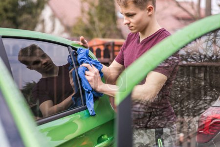 Photo for Spring cleaning. Young boy is polishing the green car. - Royalty Free Image