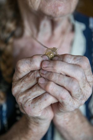 Photo for Hands of an old woman praying and holding a gold medal with Our Lady - Royalty Free Image