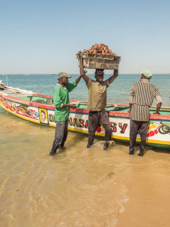 Téléchargez les photos : Sénégal, Afrique - 24 janvier 2019 : Un pêcheur porte une boîte sur la tête avec des coquillages pêchés hors de l'océan. Afrique - en image libre de droit