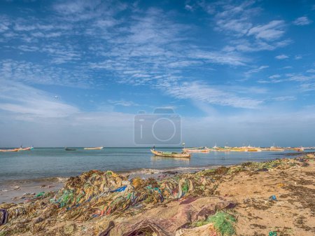 Photo for Senegal, Africa - January 26, 2019: Plenty of plastic bags on shore of the ocean. Pollution concept. Colorful fisher boats in the background. Senegal. Africa. - Royalty Free Image