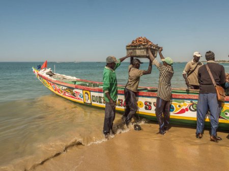 Téléchargez les photos : Sénégal, Afrique - 24 janvier 2019 : Des pêcheurs portent une boîte avec des coquillages pêchés hors de l'océan. Afrique - en image libre de droit
