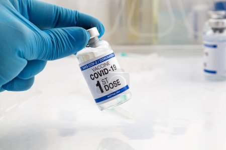 Photo for Hand holding COVID-19 Vaccine Vial for vaccination tagged with 1st dose vaccine. Doctor holding Coronavirus vaccine bottle with the name of first dose of the covid vaccine on the label - Royalty Free Image