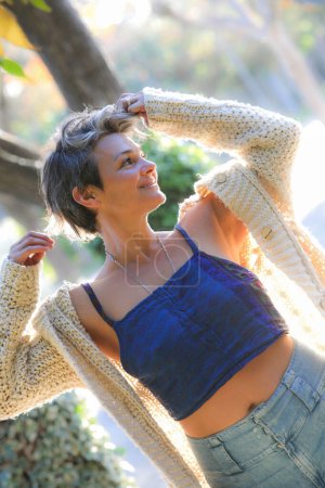 retrato de mujer joven atractiva con el pelo corto en un suéter de punto y jeans en un parque de otoño.