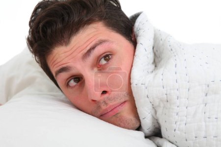 close up of a young man in bed under blanket with discontent face