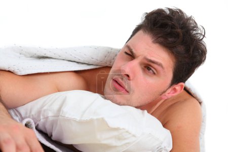close up of a young discontent man in bed waking up with tired and  annoyed  facial expression