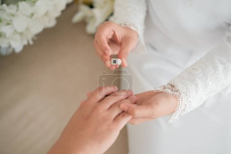Malaiisches Hochzeitspaar legt einen Ring an die Hand. Selektiver Fokus und flacher DOF.