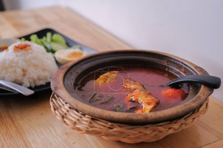 Une photo d'Ikan Kembung "asam pedas" avec du riz blanc sur un fond en bois. "Asam pedas" est une soupe aigre à base de tamarin, de piment et d'épices qui est populaire en Malaisie