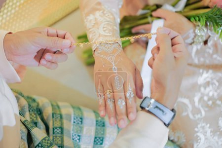 El novio está vistiendo el brazalete a la mano de la novia durante la ceremonia de boda malaya en Malasia. La mano de las novias con henna