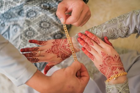 The groom is dressing the bracelet to the bride's hand during the Malay wedding ceremony in Malaysia. The brides hand with henna