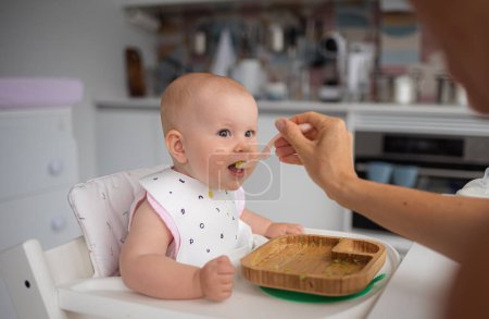 Téléchargez les photos : Bébés d'abord nourrir, maman nourrit un bébé surpris avec une cuillère. Photo de haute qualité - en image libre de droit