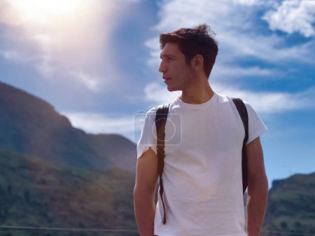 Foto de Guapo joven senderismo con mochila en exuberante paisaje de montaña verde mirando hacia otro lado - Imagen libre de derechos